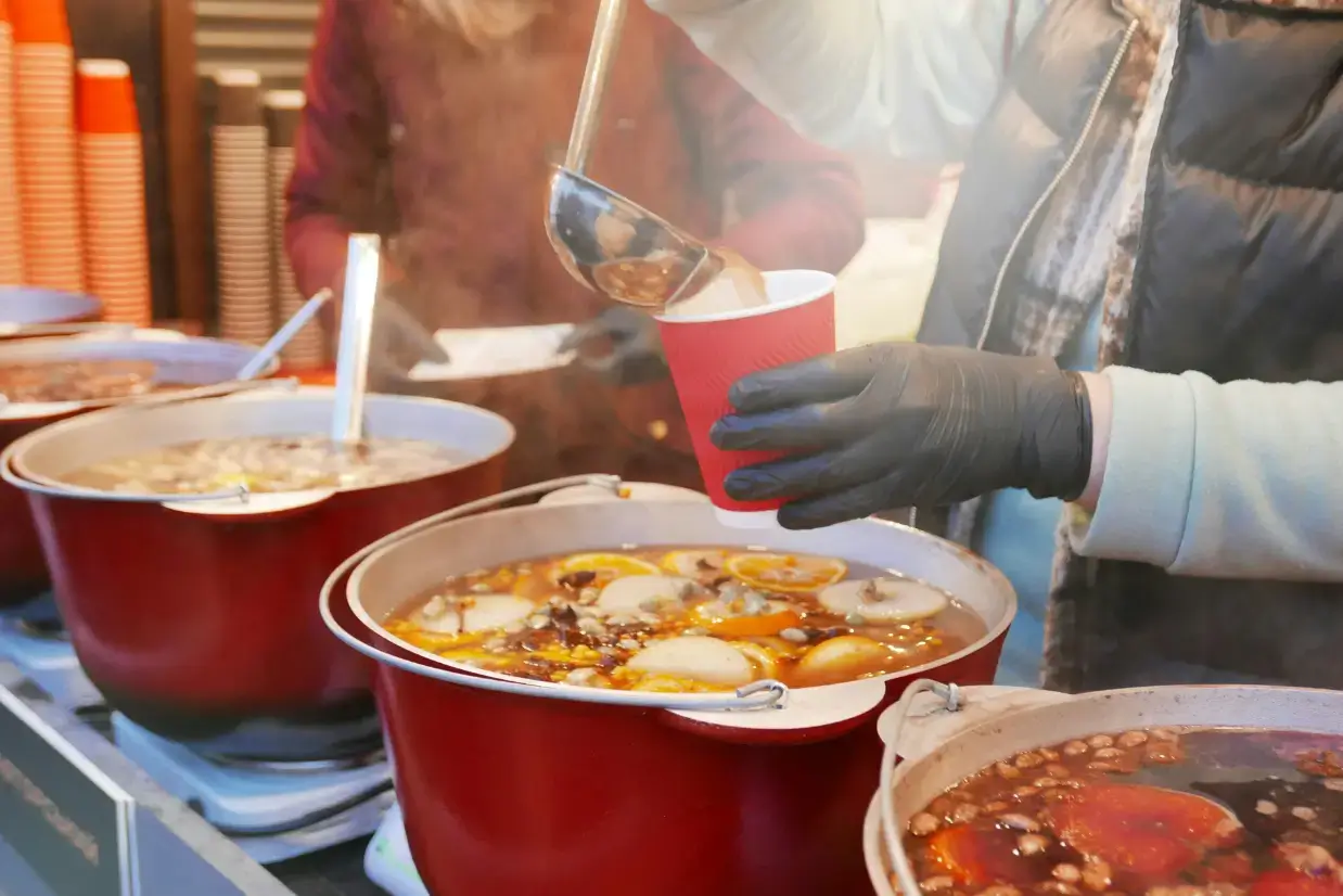 Pessoa servindo o Glühwein, vinho quente tradicional alemão, com cravo, canela, laranja e outras especiarias