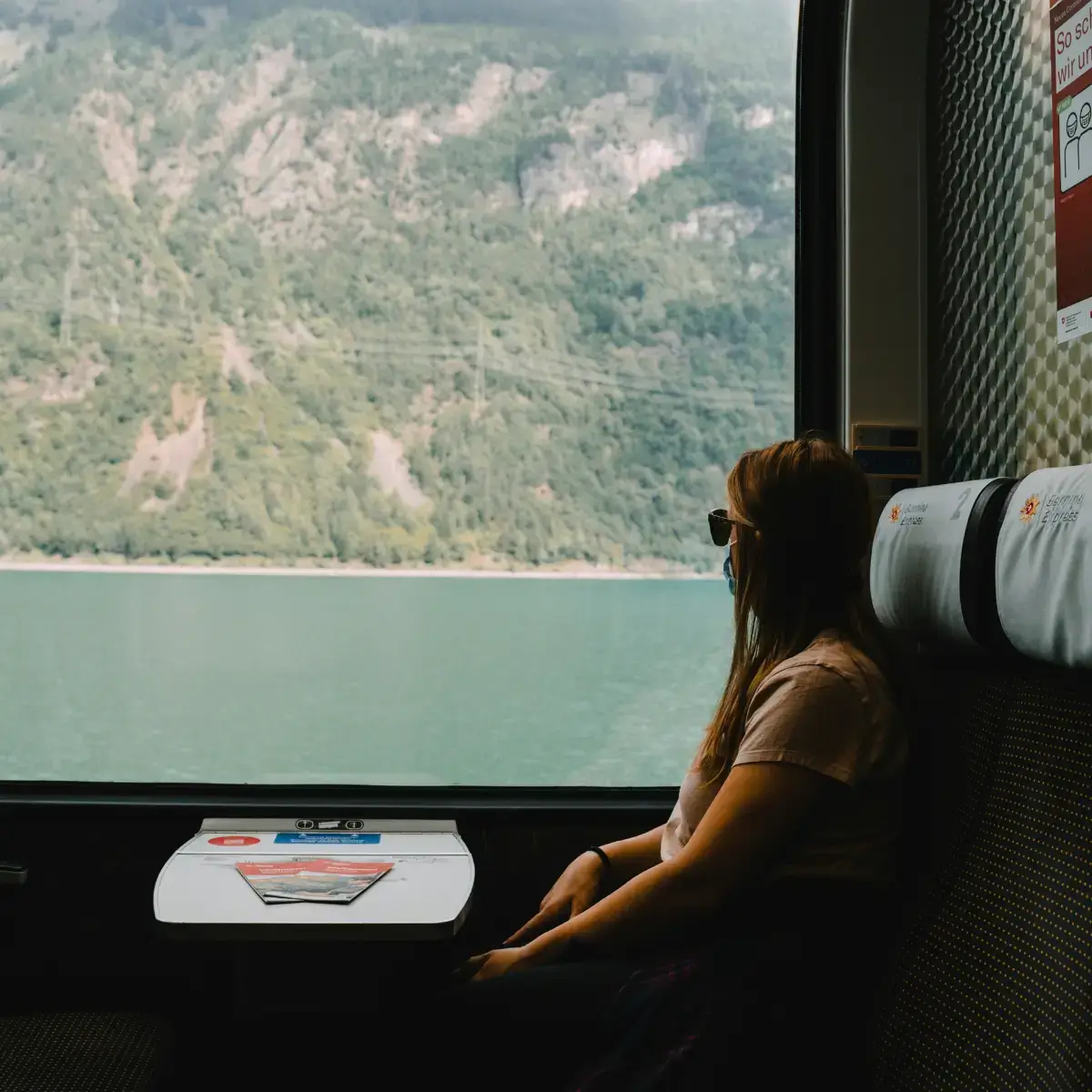 Viajante aprecia a vista da janela de um trem panorâmico pelos Alpes suíços, com montanhas verdejantes