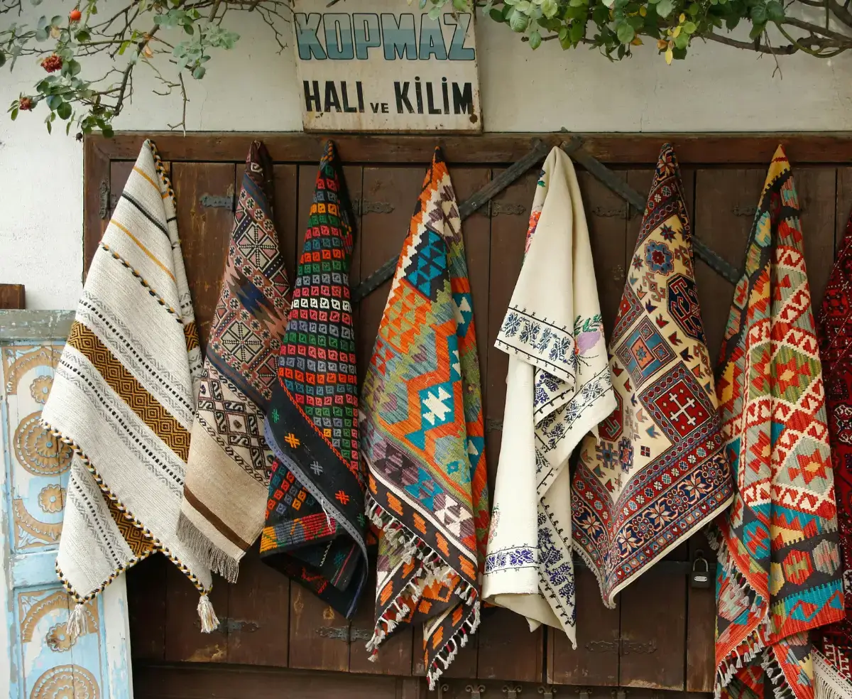 Cenário de um mercado ao ar livre com tapetes turcos otomanos expostos, com cores vivas e diferentes símbolos